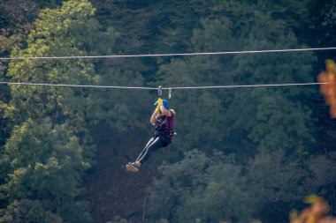 Eğlence, adrenalin ve teleferik hattında macera. Ergen, panoramik orman arka planında zeplinle eğleniyor. Ormanda halatla kayma. İnsanlar ormandaki halatla adrenalin salgılar.