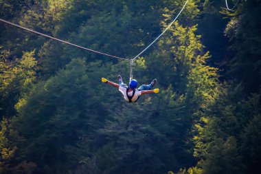 Eğlence, adrenalin ve teleferik hattında macera. Ergen, panoramik orman arka planında zeplinle eğleniyor. Ormanda halatla kayma. İnsanlar ormandaki halatla adrenalin salgılar.