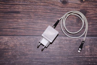 Cep telefonunu şarj etmek için bir adaptör ve USB kablosu. Masasında adaptör olan beyaz bir C tipi kablo. Tahta arka planda beyaz USB kablosu.