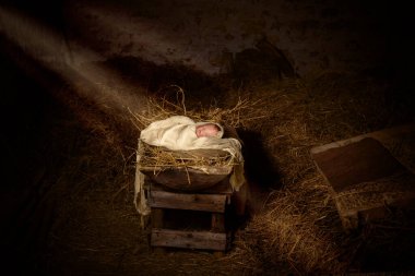 Dark stable with a doll playing jesus as a baby in the manger clipart