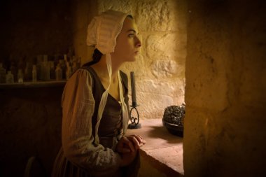 Rönesans tarzı giyinmiş genç bir kız ortaçağ şatosunun penceresinden dışarı bakıyor.