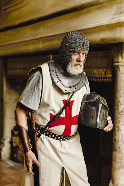 Настоящий рыцарь в средневековой одежде крестоносца со шлемом, цепной почтой и мечом