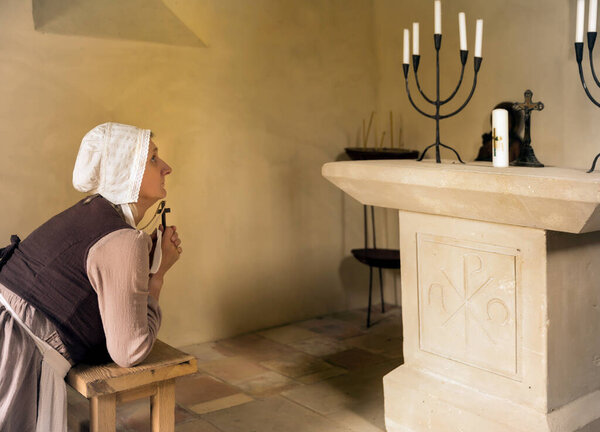 Зрелая женщина в средневековом наряде, преклоняющая колени в молитве в часовне французского средневекового замка