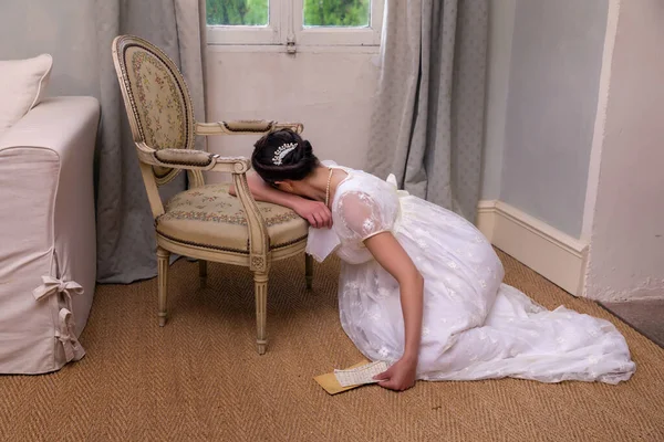 本物の摂政のドレスに若い女性を表現する手紙を保持し アンティークの椅子にもたれて — ストック写真