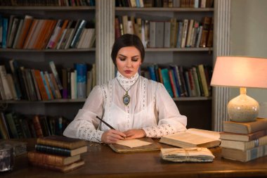 Kütüphanede oturan Edwardian etekli ve yüksek yakalı dantel bluzlu güzel bayan. Öğretmen de olabilir, müdire de..