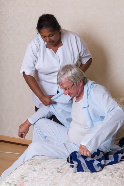 Sjuksköterskan att hjälpa äldre man att få klädd — Stockfoto
