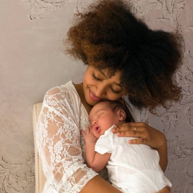 Güzel Afrikalı Etiyopyalı genç anne yeni doğmuş bebeğini kucağında tutuyor ve beyaz dantel bir gecelik ya da elbise giyiyor.