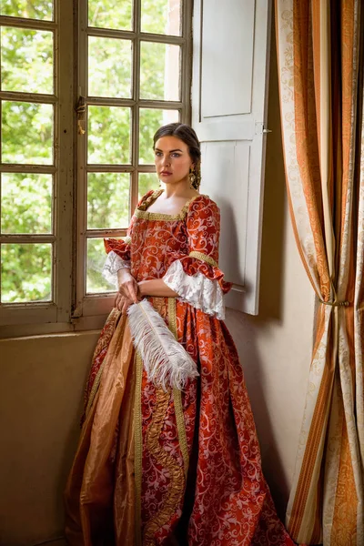 Otantik Rönesans kostümü ve başlık giymiş bir kadın ortaçağ şatosunun penceresinde dikiliyor.