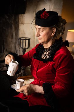 Kırmızı ve siyah kadife kadife elbiseli kadın 18. yüzyılda iç mekanda poz vermiş.