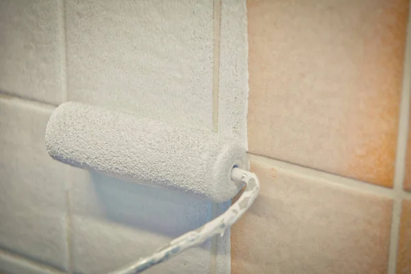 Painting old tiles in the kitchen or bathroom white with a small roller and two component paint. Interior renovation.