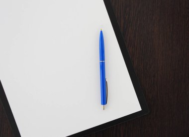 Ahşap masanın üzerinde duran mavi kalem ve boş kağıt.
