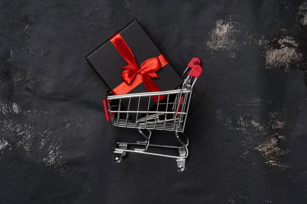 Carro de la compra con caja de regalo y hacer frente al espacio sobre fondo negro —  Fotos de Stock