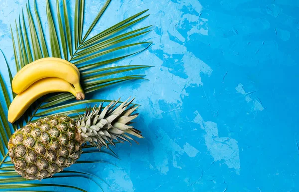 Pineapple,banana and tropical palm leave on blue cement background. Top view