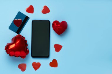 Sevgililer Günü geçmişi cep telefonu, kırmızı kalp, mevcut ve kredi kartı pastel mavi arka planda.