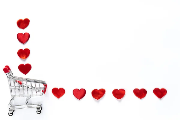 Os corações vermelhos pequenos estão caindo da cesta do carrinho de compras no fundo branco. — Fotografia de Stock