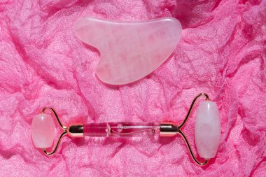Pembe Gua Sha yüz masajı aletleri. Gül arka planında Rose Quartz yeşim taşı silindiri