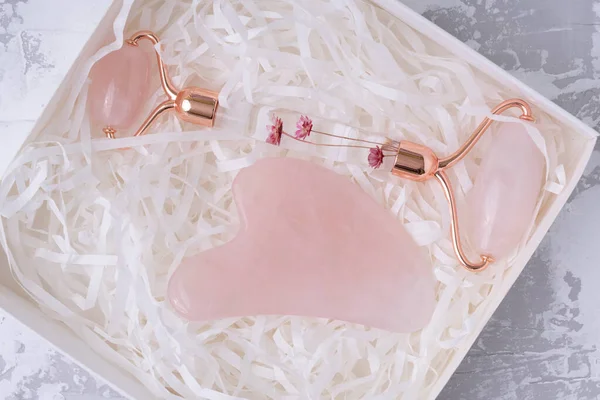 Pink Gua Sha massage tool in box on a white cement background, top view. Rose Quartz jade roller