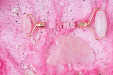 Pembe Gua Sha yüz masajı aletleri. Gül arka planında Rose Quartz yeşim taşı silindiri