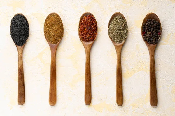 Collection of five spices on wooden spoons on yellow cement background.