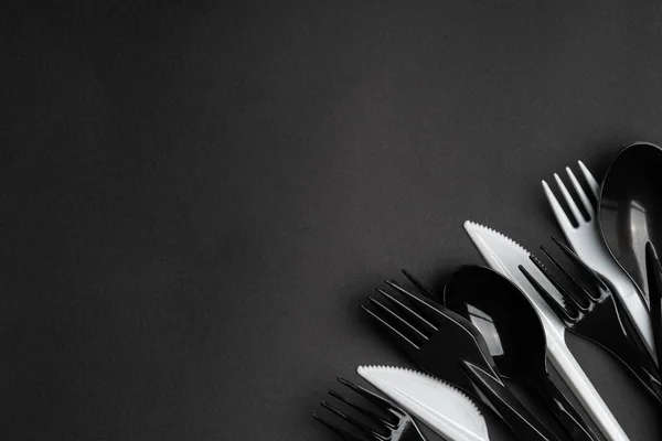 Siyah arka planda plastik beyaz ve siyah çatallar ve kaşıklar. Plastik çatal bıçak takımı, ekoloji, plastik çevre kirliliği, tek kullanımlık sofra takımı, atık geri dönüşümü konsepti. boşluk, metin yeri.