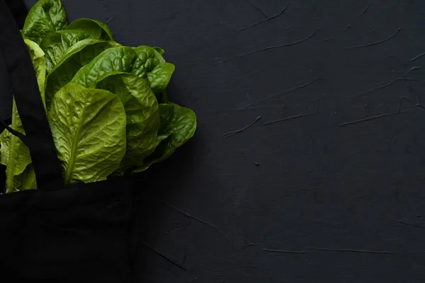 Siyah arkaplanda salata olan siyah bir alışveriş çantasının yakın plan fotoğrafı.