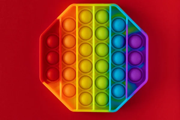 Color pop it antistress toy for children. rainbow octagon shaped isolated on red background . Pop it toy