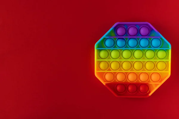 Color pop it antistress toy for children. rainbow octagon shaped isolated on red background . Pop it toy
