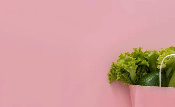 Sağlıklı beslenme geçmişi. Kağıt torba içinde vejetaryen yiyecekler pembe arka planda sebzeler. Market alışverişi ve temiz yeme konsepti.