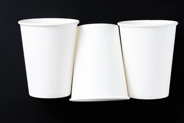 Three white paper cups of coffee on black background.Top view