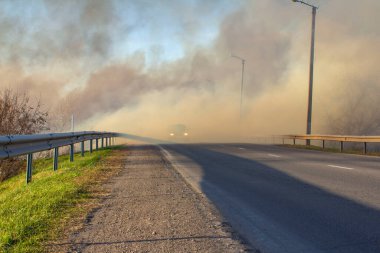 Yolun kenarındaki yangın sırasında, banliyö yolunda dumanlı bir şekilde giden bir araba.