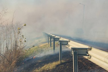 Yolun kenarındaki yangın sırasında, banliyö yolunda dumanlı bir şekilde giden bir araba.