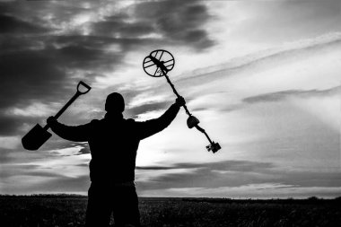 Gün batımının arka planında metal dedektörü olan mutlu bir hazine avcısı.