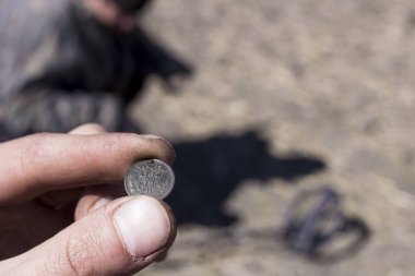 Eski bir savunma kalesinin uçsuz bucaksız genişliklerinde metal dedektörü olan bir adam antik sikkeleri ve tarihi eserleri ararken ön plan ve arka plan bokeh etkisi ile bulanıklaşır.
