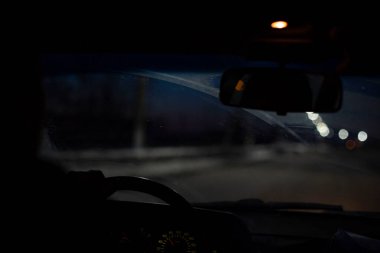 Arabanın iç tarafındaki bulanık görüş bulutlu ve kirli bir ön camdan, kötü hava koşulları ve aydınlatmada, ön ve arka plan bulanık