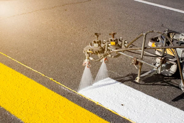 Taze asfalt üzerinde otomatik teçhizatla bahar başında yaya geçidi çizen bir grup işçi.