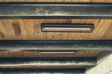 Demir kirişler arasındaki ahşap tavanda parlak lamba sergileniyor, apartman yenilenmesinin tasarım çözümünde, ön ve arka planlar bokeh etkisi ile bulanıklaşıyor