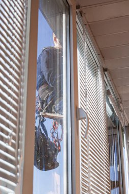 Bir endüstriyel tırmanıcı yüksek irtifa ekipmanları kullanarak bir binanın içinden fotoğraf çekiyor.