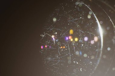 Kameranın merceğindeki çizikler ve tozdan oluşan bir yakın plan, bir lambanın arka planındaki siyah arka plan