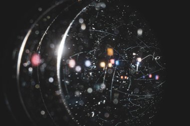 Kameranın merceğindeki çizikler ve tozdan oluşan bir yakın plan, bir lambanın arka planındaki siyah arka plan