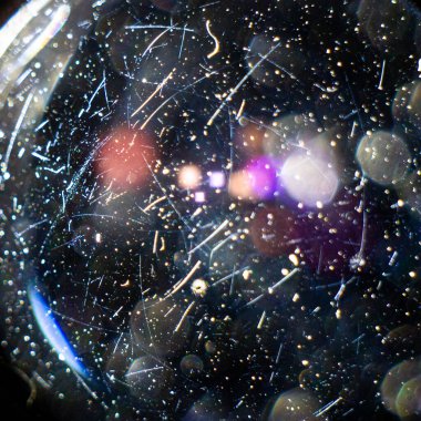 Kameranın merceğindeki çizikler ve tozdan oluşan bir yakın plan, bir lambanın arka planındaki siyah arka plan