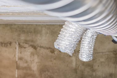 Kirli bir havalandırma deliğinin ve binanın tavanına bağlı esnek bir kanalın yakından görüntüsü. Havalandırmada önemli toz ve kir birikimi izleri var..