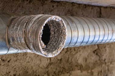 Kirli bir havalandırma deliğinin ve binanın tavanına bağlı esnek bir kanalın yakından görüntüsü. Havalandırmada önemli toz ve kir birikimi izleri var..