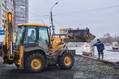 Perm, Rusya - 08 Kasım 2020: Yağmurlu havada bir sokak yolunun yeniden inşası sırasında kepçe doldurucu