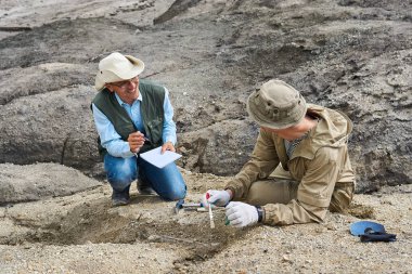 Çöldeki iki erkek paleontolog, bulguları tartışıyor ve bir not defterine not alıyorlar.