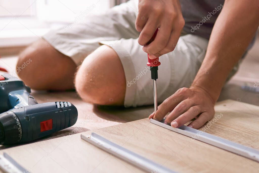 man assembles furniture by hand at home, sitting on the floor, only hands with a screwdriver in focus