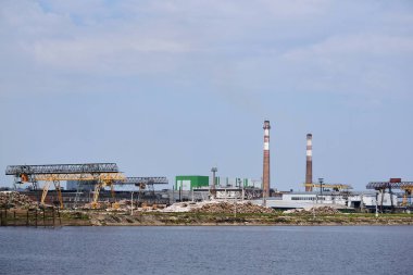 Endüstriyel peyzaj, hamuru ve kağıt fabrikası, nehir kenarındaki odun yığınları ve bacaları.