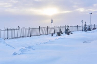 Çitleri, fenerleri, köknar ağaçları ve bulutlarda parlayan güneş ışığıyla kaplı kış parkı.