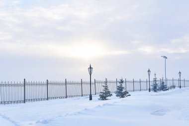 Çitleri, fenerleri, köknar ağaçları ve bulutlarda parlayan güneş ışığıyla kaplı kış parkı.