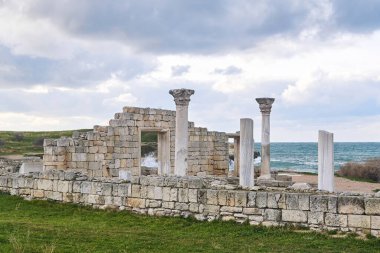 Kıyıdaki deniz dalgalarının arka planında sütunları olan antik bir bazilikanın kalıntıları.