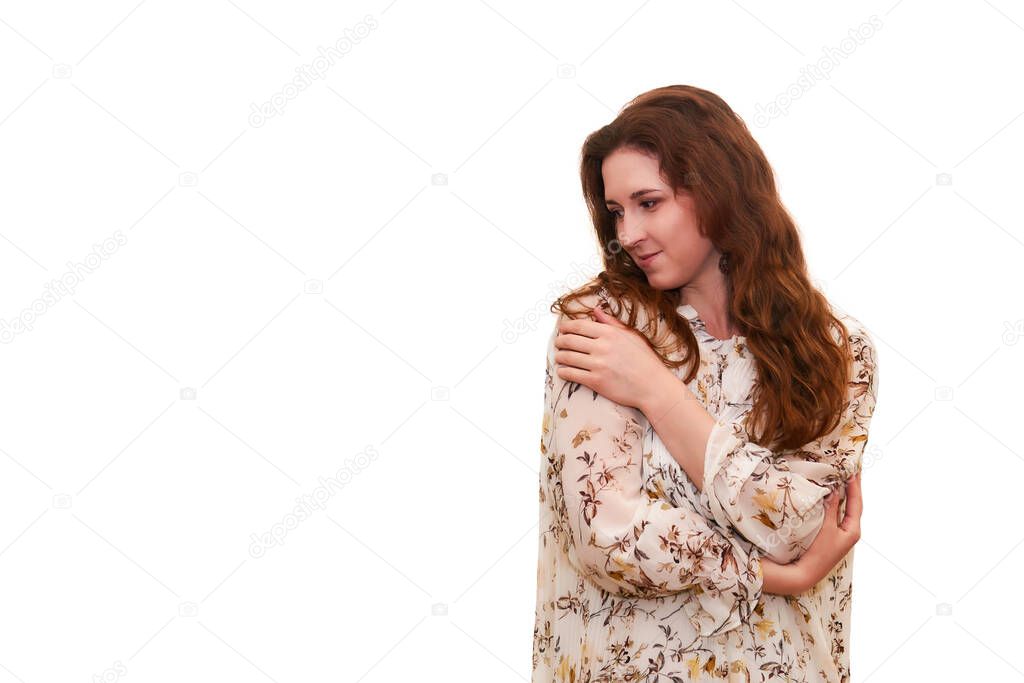 young attractive woman looks thoughtfully to the side, clasping herself with her arms, isolated on white backgroun